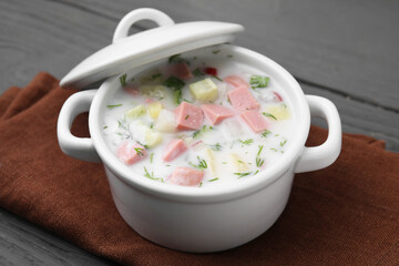 Delicious cold summer soup (okroshka) with boiled sausage in pot on grey table, closeup