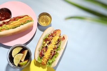 Delicious hot dogs with bacon, lettuce, onion and pickle served on light blue table, flat lay. Space for text