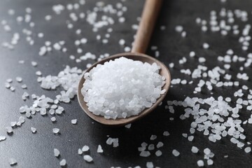 Natural salt and wooden spoon on black table, closeup