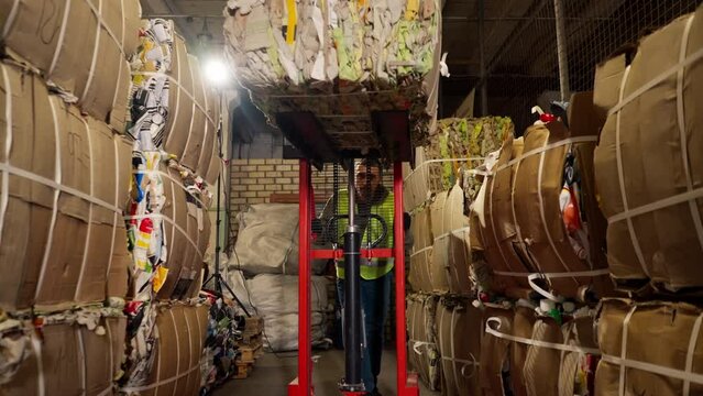 A worker using a stacker lifts and transports a cargo cardboard box with things for recycling at garbage station