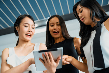 Three Asian women friends having conversation while looking at tablet computer in their hands....