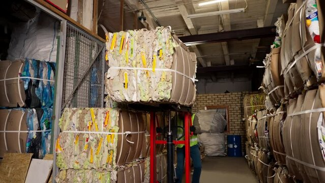 A worker using a stacker lifts and transports a cargo cardboard box with things for recycling at garbage station