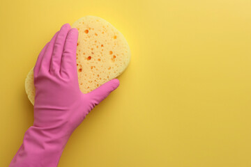 Cleaner in rubber glove holding new sponge on yellow background, top view. Space for text
