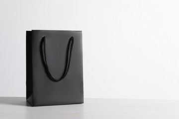 Black paper bag on white wooden table, space for text