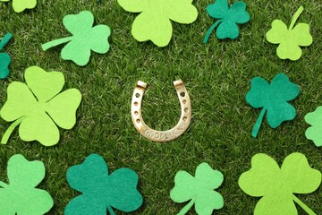 St. Patrick's day. Golden horseshoe surrounded by felt clover leaves on green grass, flat lay
