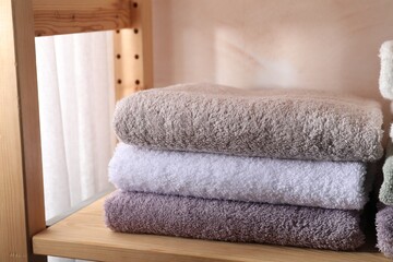 Obraz na płótnie Canvas Stacked soft towels on wooden shelf indoors