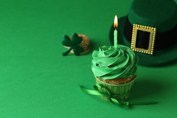St. Patrick's day party. Tasty cupcake with burning candle and leprechaun hat on green background....