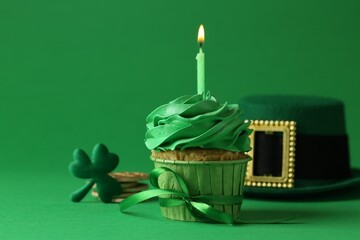 St. Patrick's day party. Tasty cupcake with burning candle and leprechaun hat on green background,...