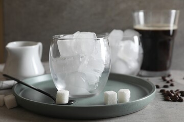 Making iced coffee. Ice cubes in glass, ingredients and spoon on gray table, closeup