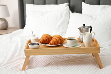 Wooden tray with tasty breakfast on bed at home