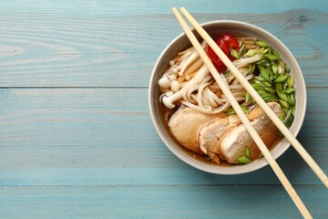 Delicious ramen with meat in bowl and chopsticks on light blue wooden table, top view. Space for...