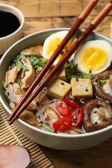Bowl of delicious ramen and chopsticks on wooden table, closeup. Noodle soup