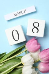 International Women's day - 8th of March. Wooden block calendar and beautiful flowers on light blue background, flat lay