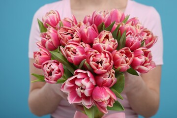 Woman holding beautiful bouquet on light blue background, closeup