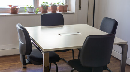 Modern office meeting room with white table, comfortable chairs, and potted plants by the window; concept of corporate, work environment.