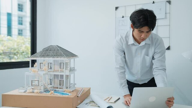 Close up of professional male architect engineer measure house model and using laptop analysis data at meeting table with house model and map . scatter around. Focus on hand. Immaculate.