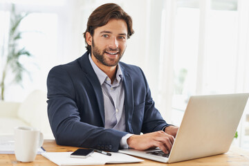 Obraz premium Portrait, laptop and smile with business man at desk in office, working on corporate review or feedback. Computer, email or research with happy young employee typing report for info in workplace