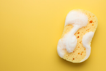 Sponge with foam on yellow background, top view. Space for text