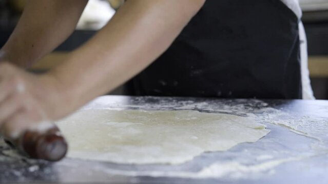 baker kneading bread dough with a rolling pin on a grey workbench, traditional cuisine