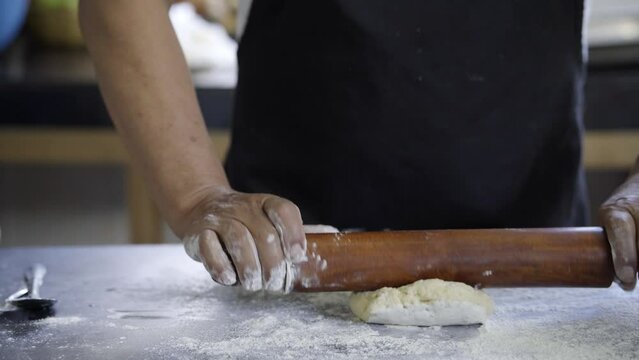 baker kneading bread dough with a rolling pin on a grey workbench, traditional cuisine