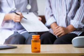 bottle of pills, Doctor explains reports health examination results to patient woman on sofa at...