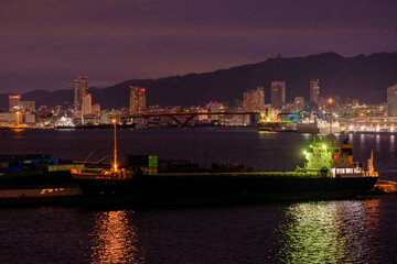 Fototapeta na wymiar 夜の神戸の港。六甲大橋から三宮のビル街をのぞむ。背景は六甲の山並みがシルエットで浮かぶ。