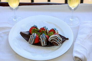 Chocolate covered strawberries on a chocolate leave tray and view of champagne glasses.