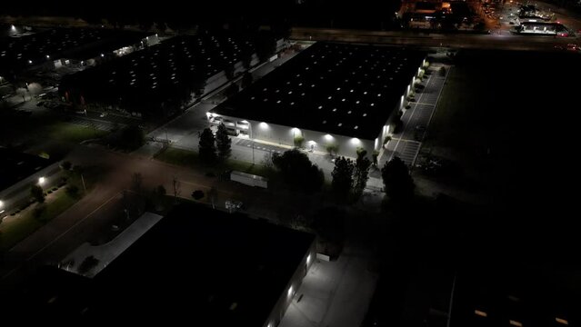 An industrial warehouse building with skylights on the roof is shown from an aerial flyover view at night.