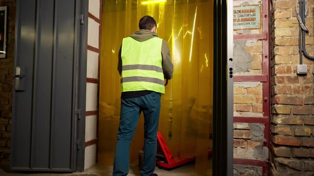 A worker at a waste processing plant in a work vest passes through a silicone curtain at the door of a waste sorting plant