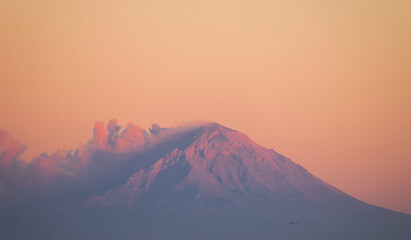 Volcán con una erupción de ceniza durante un atardecer de colores pastel
