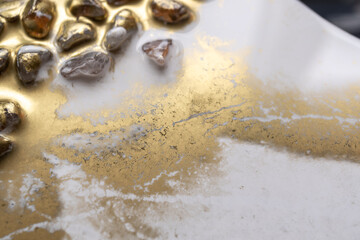 tabla trabajada con resina epóxica pigmentada con polvo dorado y piedras de adorno, acercamiento.
