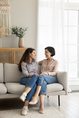 Vertical shot elderly woman spend time lead conversation with lovely young adult daughter. Millennial Hispanic female enjoy talk, trustworthy communication with caring mature mother seated on couch