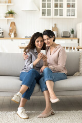Obraz premium Multigenerational women, mom and daughter doing online shopping using cellphone, sitting on cozy sofa in studio flat, choose goods, enjoy remote purchases using mobile application, marketplace website