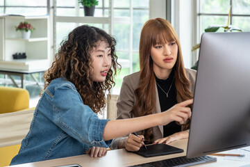Two young Asian female woman businessperson graphic designer working together, meeting and brainstorming, using computer in office, pointing at screen.