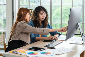 Two young Asian female woman businessperson graphic designer working together, meeting and brainstorming, using computer in office, pointing at screen.