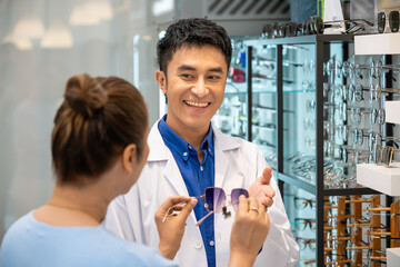 Young Asian male man optician explaining and selling eyeglasses to senior female woman customer in optical shop store. Eyecare concept.