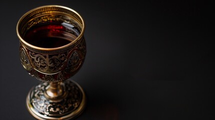 An ornate wine cup used in the Kiddush ceremony at the beginning of the holiday, filled with red wine. black background