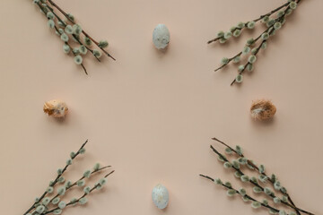 flat lay photo of fluffy willow branches and Easter eggs in pastel shades on a beige background. an...