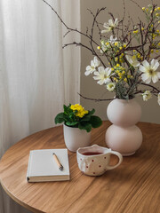 A gratitude journal, a cup of tea, flowers on a round wooden table. Daily ritual, cozy house concept