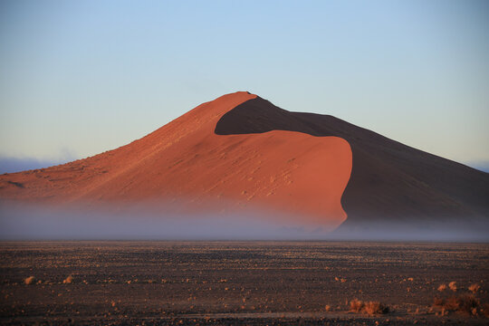 massive red sand dune of Namib desert with a layer of fog at the base