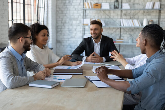 Happy employees and CEO in modern workspace. Multiracial sales team having meeting with director. Young professionals discussing work issues, analyzing financial statistics, sharing ideas