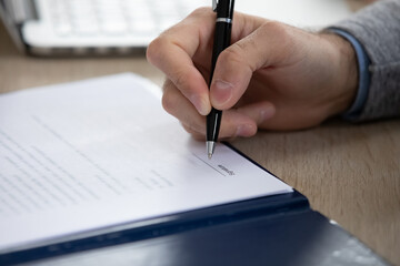 Close up of male client putting signature on will or bank agreement. Focus on hand of lawyer...