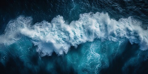 A powerful surging wave of the sea is depicted in this breathtaking aerial image as it crashes into a frothy foam against the dark depths below, evoking a sense of wonder and strength.