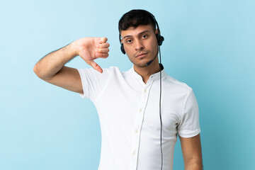 Telemarketer Colombian man working with a headset over isolated background showing thumb down with...