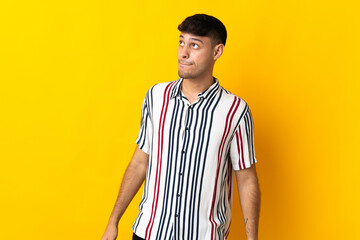Young Colombian man isolated on yellow background having doubts while looking up