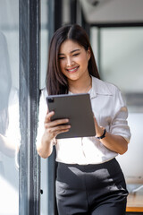 Fototapeta premium Young asian busy professional business woman executive, female company worker or manager holding digital tablet technology device working standing in modern corporate office.