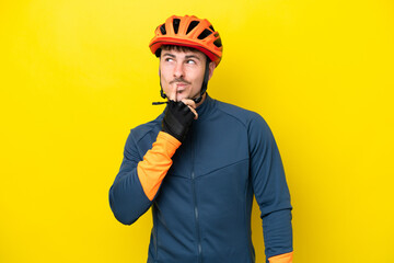 Young cyclist caucasian man isolated on yellow background having doubts while looking up