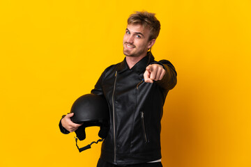 Man with a motorcycle helmet isolated on yellow background pointing front with happy expression