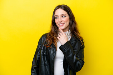 Young caucasian woman isolated on yellow background looking up while smiling