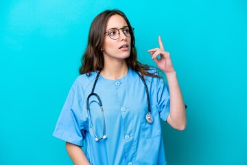 Young surgeon doctor woman isolated on blue background thinking an idea pointing the finger up